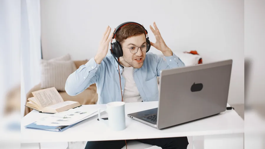 Mann mit Brille schreit am Schreibtisch mit offenem Mund vor seinem Laptop